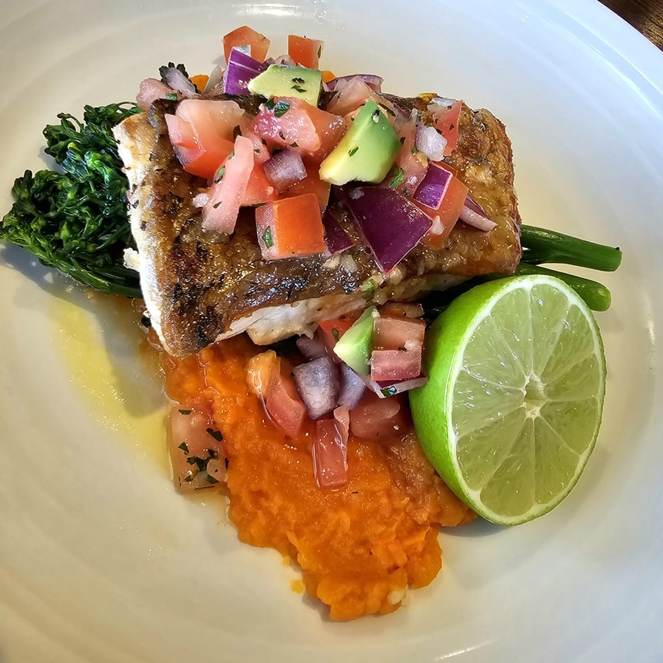 Pan-seared fish with tomato, avocado, and red onion salsa, served with broccolini, sweet potato mash, and a lime wedge.
