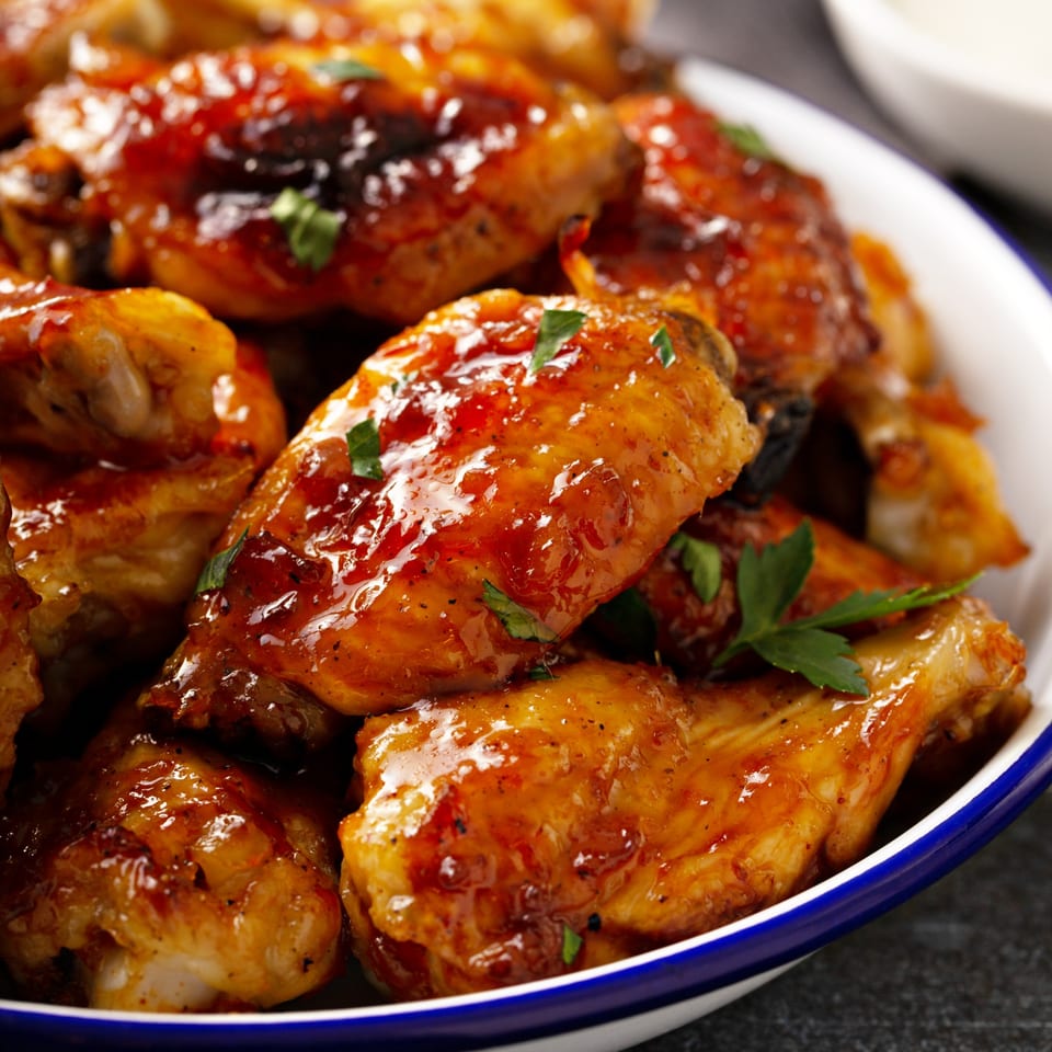 Close-up of Kings Duck Bar&Grill's glazed chicken wings, garnished with fresh parsley in a white bowl.