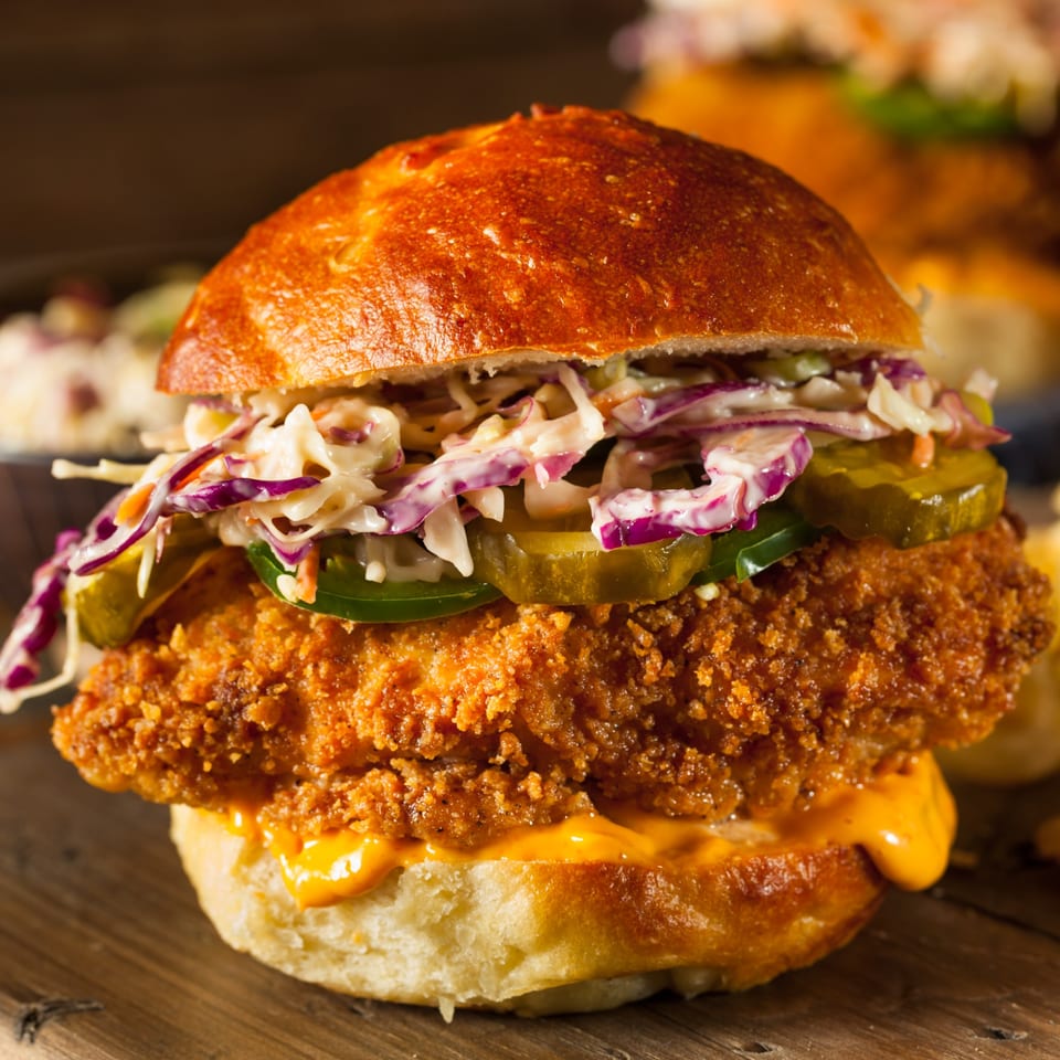 Kings Duck Bar&Grill's crispy fried chicken sandwich with coleslaw, pickles, and jalapeños on a brioche bun.